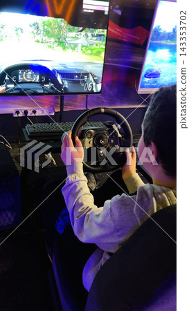 Teenager playing a car driving simulator in an arcade. 143353702