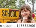 Young smiling girl is posing outside in front of a yellow school bus. 143353966