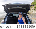 Woman is sitting in the trunk of her car by the seaside. Horizontally. 143353969