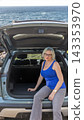 Woman is sitting in the trunk of her car by the seaside. Vertically. 143353970