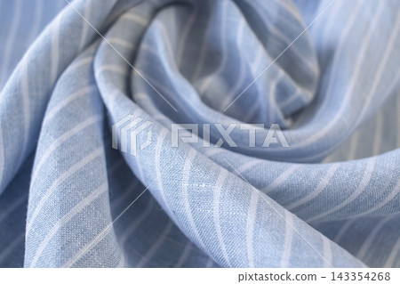 Natural linen fabric. Draped light blue fabric with white stripes. Texture of blue-and-white striped linen fabric with soft folds. Natural linen fabric. Draped light blue fabric with white stripes. Texture of blue-and-white striped linen fabric with soft folds. 143354268
