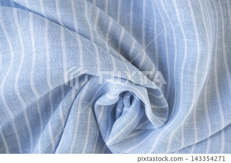 Natural linen fabric. Draped light blue fabric with white stripes. Texture of blue-and-white striped linen fabric with soft folds. 143354271