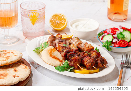 Souvlaki, a Greek dish, grilled meat shish kebab, on a plate with flatbreads, and lemon slices, grilled meat shish kebab, served with lavash, salad and drinks where there are no people Souvlaki, a Greek dish, grilled meat shish kebab, on a plate with flatbreads, and lemon slices, grilled meat shish kebab, served with lavash, salad and drinks where there are no people 143354395