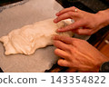 Hands shaping homemade pizza dough on parchment paper 143354822