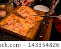 Hands slicing pizza with a kitchen knife on wooden board. Shared pizza meal and food preparation. Italian cuisine, casual dining and home cooking. Group dining and meal sharing. 143354826