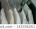 Macro photography of tightly hanging white and mint blouses with embossed small patterns and structural shoulders on multi-colored plastic hangers. Concept: focus on the texture of the material and 143356261