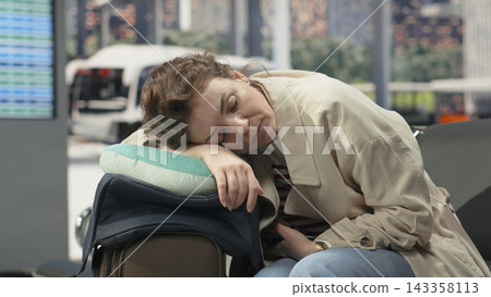 Close up of woman in bus station sleeping on neck pillow on top of trolley. Weary traveler putting head on baggage, closing eyes to recover, easing fatigue after long time on road Close up of woman in bus station sleeping on neck pillow on top of trolley. Weary traveler putting head on baggage, closing eyes to recover, easing fatigue after long time on road 143358113