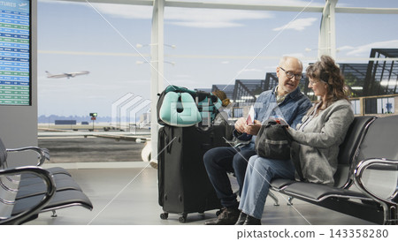 Joyful older adults relaxing in airport terminal engaged in discussion before boarding plane. Mature couple enjoying travel lifestyle, representing active global travel and sightseeing. 143358280