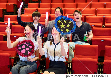 A group of men and women enjoying their fan activities at the theater, holding penlights and fans. A group of men and women enjoying their fan activities at the theater, holding penlights and fans. 143358711