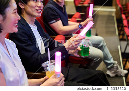 觀眾在劇院裡欣賞現場表演，手裡拿著螢光棒和飲料。 143358820