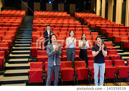 The audience gives a standing ovation in the theater, smiling and applauding. The audience gives a standing ovation in the theater, smiling and applauding. 143359539