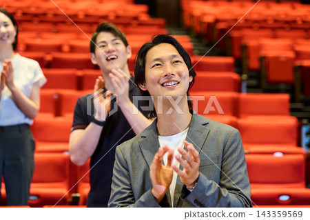 The audience gives a standing ovation in the theater, smiling and applauding. The audience gives a standing ovation in the theater, smiling and applauding. 143359569