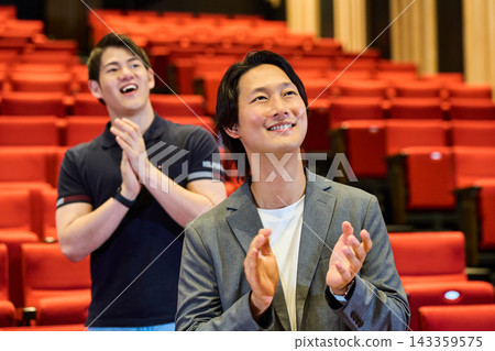 The audience gives a standing ovation in the theater, smiling and applauding. The audience gives a standing ovation in the theater, smiling and applauding. 143359575