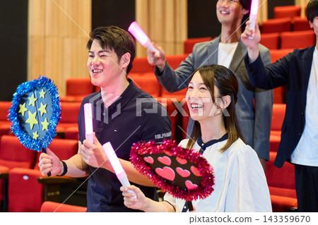 男男女女站在劇院裡，手持螢光棒和扇子，享受他們的扇子活動。 143359670