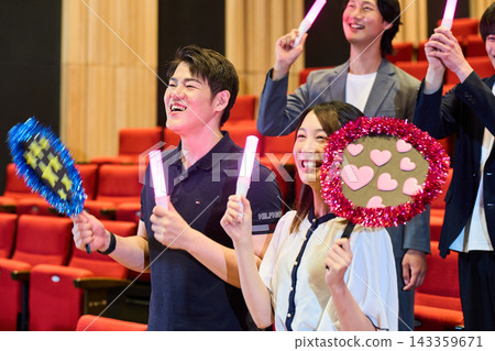 Men and women standing in the theater, holding penlights and fans, enjoying their fan activities. Men and women standing in the theater, holding penlights and fans, enjoying their fan activities. 143359671
