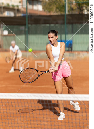 Two women in sportswear spending time playing sports on tennis courts, young girl receiving hit from tennis racket Two women in sportswear spending time playing sports on tennis courts, young girl receiving hit from tennis racket 143360226