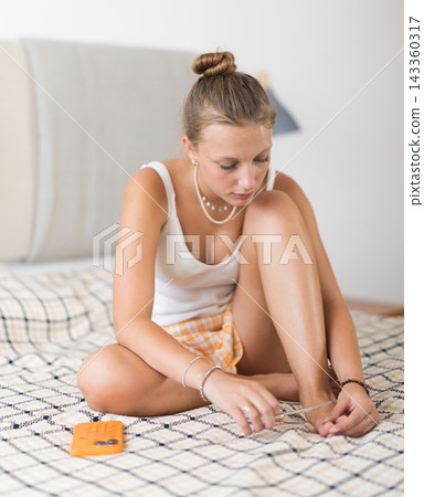 Young woman doing pedicure sitting on bed in bedroom Young woman doing pedicure sitting on bed in bedroom 143360317