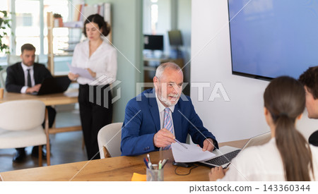 Professional mature male lawyer or bank manager talking with young couple and helping opening account in bank at office Professional mature male lawyer or bank manager talking with young couple and helping opening account in bank at office 143360344
