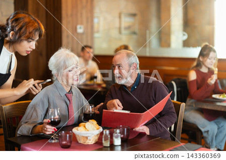 Young female waitress takes order from elderly couple Young female waitress takes order from elderly couple 143360369