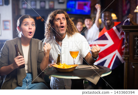 Happy male and female holding the flag of Great Britain, supporting national football team in the bar 143360394
