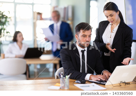 Woman head of a bank office stands with a male employee and helps with work issues Woman head of a bank office stands with a male employee and helps with work issues 143360560