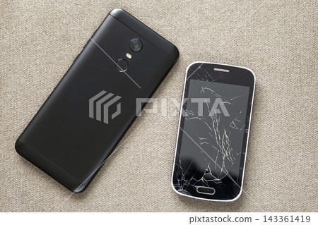 Comparison of two black mobile phones, old cellphone with cracked screen and new modern on light cloth copy space background. Technology progress and replacement concept. Comparison of two black mobile phones, old cellphone with cracked screen and new modern on light cloth copy space background. Technology progress and replacement concept. 143361419