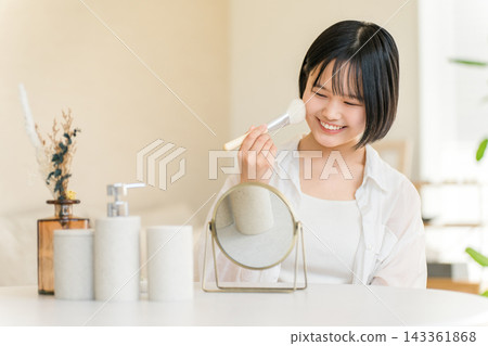 一位十幾歲的女孩對著鏡子用刷子塗腮紅；一位年輕的高中女生正在化妝。 143361868