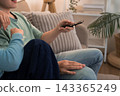 Young couple relaxing on sofa holding remote control while watching television together at home 143365249
