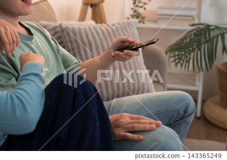 Young couple relaxing on sofa holding remote control while watching television together at home Young couple relaxing on sofa holding remote control while watching television together at home 143365249