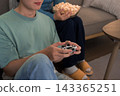 Young Asian man holding game controller while partner eats popcorn watching TV together at home 143365251