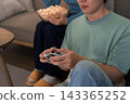 Young Asian couple sharing popcorn while playing video game together on sofa at home 143365252