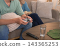 Asian couple relaxing on sofa playing video game together with popcorn and water glass nearby 143365253