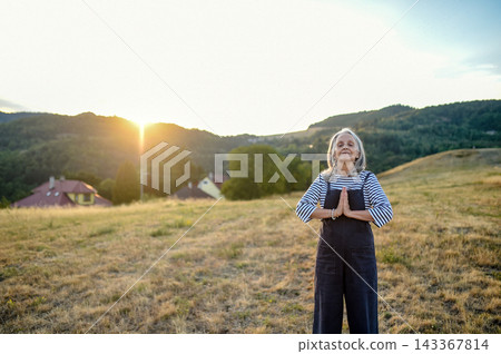 Senior woman practicing meditation outdoors in peaceful countryside. 143367814