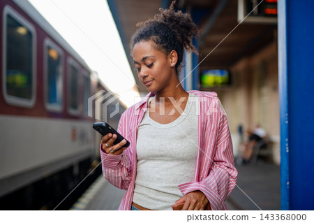 Female college student waiting for train, scrolling on phone. Female college student waiting for train, scrolling on phone. 143368000