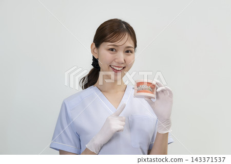 一位牙齒衛生員面帶微笑地看著鏡頭,手裡拿著她戴著牙套的牙齒印模。 一位牙齒衛生員面帶微笑地看著鏡頭,手裡拿著她戴著牙套的牙齒印模。 143371537