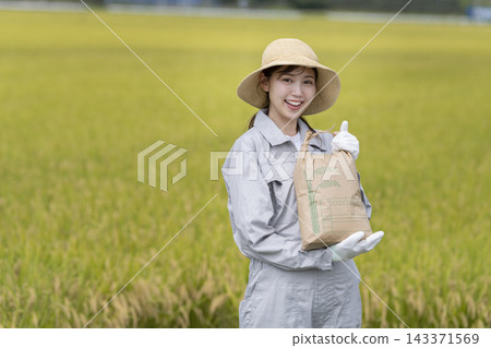 A female farmer smiling at the camera while holding a rice bag. A female farmer smiling at the camera while holding a rice bag. 143371569