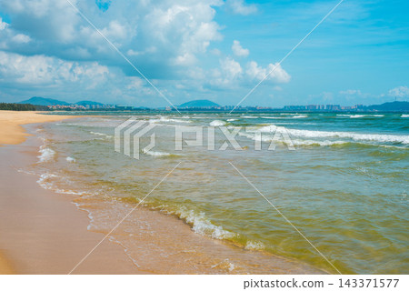 Sanya Hainan travel destination view. Sand beach, ocean waves, and cityscape on the horizon at summer day in Haitang Bay Sanya Hainan travel destination view. Sand beach, ocean waves, and cityscape on the horizon at summer day in Haitang Bay 143371577