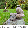 Stone balance and equilibrium concept on a green grass lawn with an ancient looking carved stone head face sculpture in a public park. 143372488