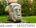 Stone face sculpture in a green park: ancient style carved rock art for landscape design and historical concepts 143372493