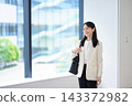 一位笑容燦爛的女員工站在辦公室窗邊微笑。 143372982