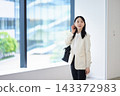 身著辦公休閒裝，站在辦公大樓窗邊 143372983