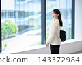 一位年輕的女上班族站在辦公室窗邊，凝視著窗外。 143372984