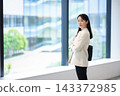 一名女上班族雙手交叉，站在辦公大樓的窗邊。 143372985