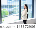 一位女上班族在燈火通明的辦公室裡，倚窗微笑。 143372986
