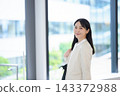 一位身穿西裝的年輕女子在辦公大樓裡微笑。 143372988
