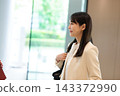 一位女商人面帶微笑，在辦公大樓大廳與人交談。 143372990