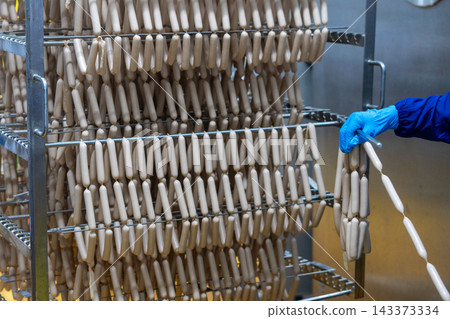 Rows of Fresh Sausages Hanging on Racks in Food Processing Factory Rows of Fresh Sausages Hanging on Racks in Food Processing Factory 143373334