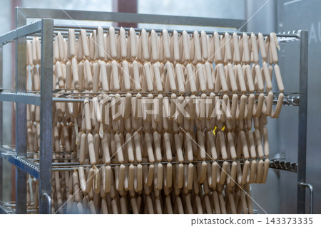 Rows of Fresh Sausages Hanging on Racks in Food Processing Factory Rows of Fresh Sausages Hanging on Racks in Food Processing Factory 143373335
