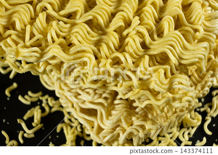 Dry instant wavy noodles with small pieces on dark background. Dry instant wavy noodles with small pieces on dark background. 143374111