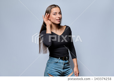 Curious young woman holding hand near ear and listening carefully Curious young woman holding hand near ear and listening carefully 143374258